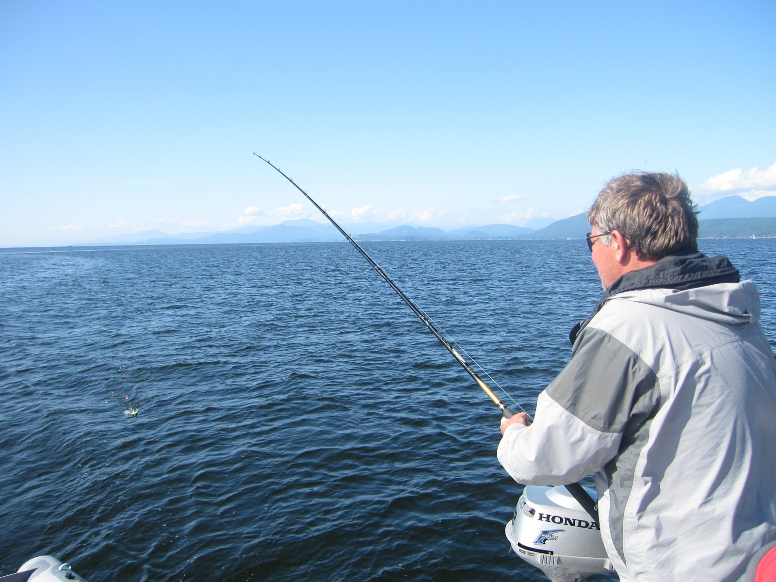 Todd on the boat, rod bent into a fish, mountains across the water